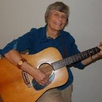 Dianne Baker holding an acoustic guitar and smiling